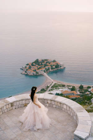 The bride stands on the observation deck overlooking the island of Sveti Stefan, back viewの写真素材
