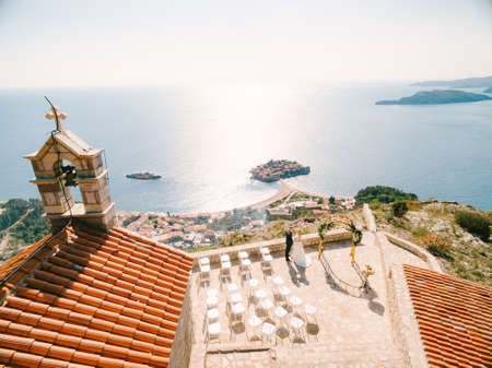 Bride and groom stand on the observation deck in front of the Sveti Sava church overlooking the Sveti Stefan island. Montenegro. View from aboveの写真素材