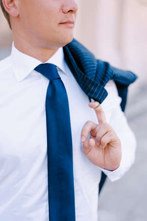 Man in a white shirt holds a jacket hanging on his shoulder with his fingerの写真素材