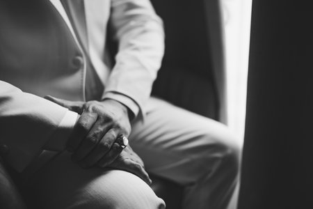 A man in a suit with a signet ring on his little finger sits by the window, close-up, black and whiteの写真素材