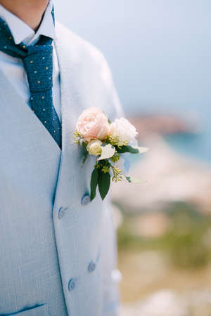 A man in a blue vest, blue tie and a delicate boutonniere with roses and eucalyptus, close-upの写真素材