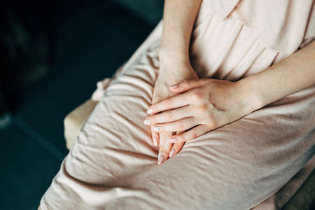 Woman in a beige dress folded her hands in her lap, sitting on a chair. Close-upの写真素材
