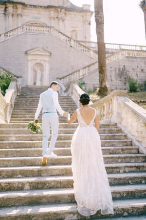 The bride and groom climbing the stairs of the Nativity of the Blessed Virgin Mary church in Prcanj and holding handsの写真素材