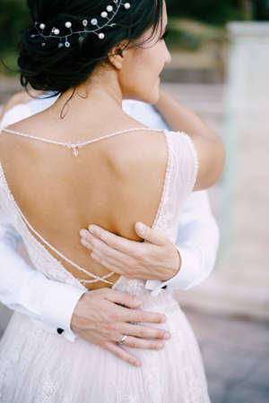 The groom gently hugs the bride in stylish dress with open back. Hands of the groom on the waist of the bride, close-upの写真素材