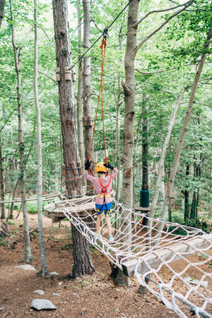 Boy walks on a mesh bridge, holding on to a safety ropeの写真素材