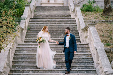 Bride and groom descend the steps holding handsの写真素材