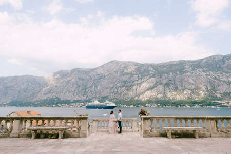 Groom and bride stand on the embankment of the bay against the background of the mountains