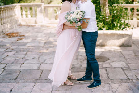 Groom hugs bride with a bouquet of flowersの写真素材