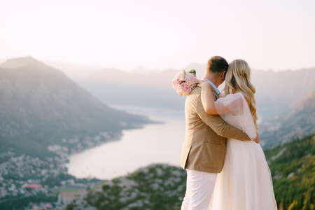 Bride and groom are hugging each other on the mountain and look at the bayの写真素材