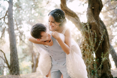The bride jumped onto the grooms back. The bride and groom are having fun among the trees in the olive groveの写真素材