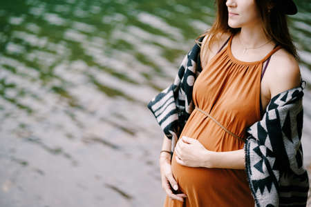 Pregnant woman in a hat stands by the lake. Close-upの写真素材