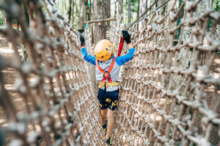 Boy walks across a mesh bridge, holding onto a cable. Back viewの写真素材