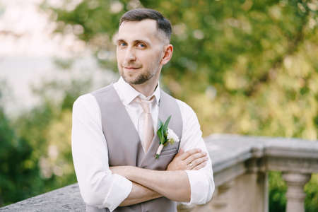 Groom crossed his arms over his chest near the balustrade in the garden. Portraitの写真素材