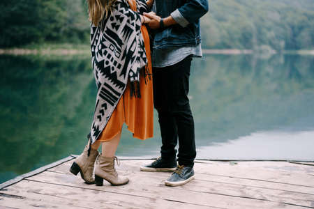 Pregnant woman and a man stand on a pier by the lake. Close-upの写真素材