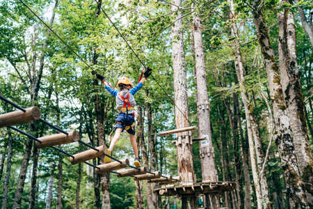 Boy walking on the agility bridge to the wooden platform holding on to the ropesの写真素材
