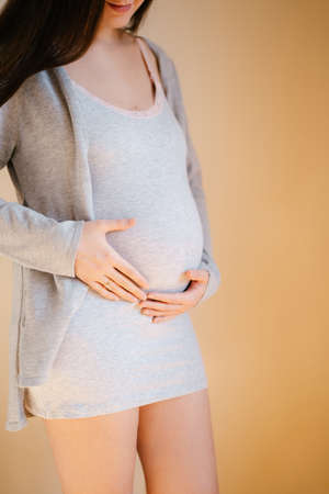 Pregnant woman stands by the wall holding her tummy