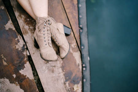 Female feet in high heel boots on a wooden pier above the water. Close-upの写真素材