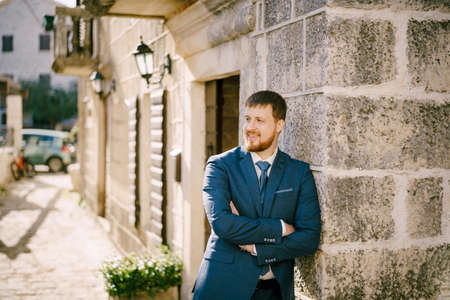 Smiling bearded red-haired man leaning against the wall of an old stone houseの写真素材