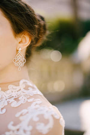 Beautiful openwork precious earring in the ear of the bride in a white dress. Close-upの写真素材