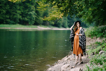 Pregnant woman stands on a rocky lake shore in the forestの写真素材
