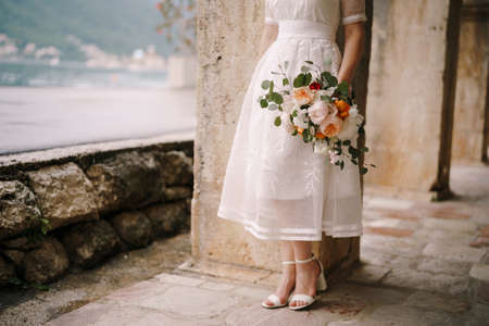 Bride with a bouquet of flowers stands near a column on the coast. Close-upの写真素材
