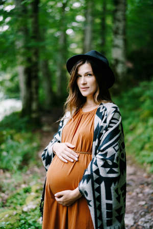 Pregnant woman in hat hugs belly with hands in green parkの写真素材