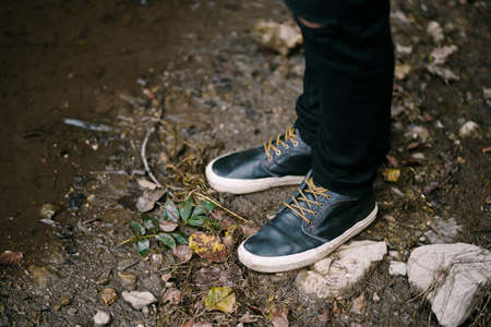 Male feet in black sneakers are on the ground near the water. Close-up