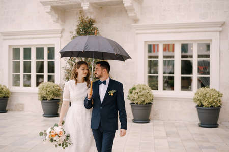 Bride and groom with an umbrella in the courtyard of an old villaの写真素材
