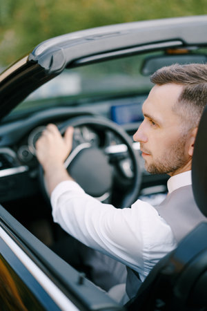 Man in a white shirt and vest sits at the wheel of a convertible. Back view. Close-upの写真素材