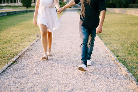 Man and woman walking along the gravel path in the park holding handsの写真素材