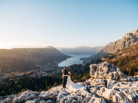 Bride and groom stand hugging each other on the top of the mountain and look at the valleyの写真素材