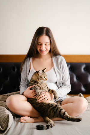 Pregnant woman sitting on bed with catの写真素材
