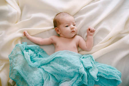 Newborn lies on a beige blanket covered with a blue scarfの写真素材