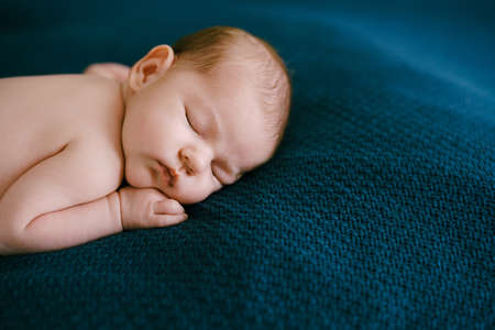 Naked baby sleeping on a blue blanket with his hand under his cheekの写真素材