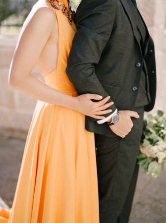 Woman in a yellow dress hugs man from behind with a bouquet. Close-up