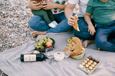 Man and woman with children on the beach sit on a blanket with foodの写真素材
