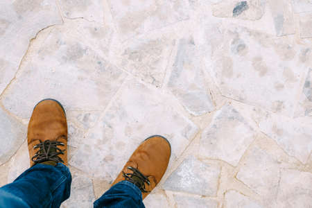 Male feet in brown boots and blue jeans on light stone tiles. Close-upの写真素材