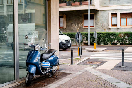 Blue motor scooter with a striped helmet is parked on paving stones near a glass showcaseの写真素材