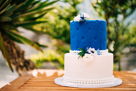 White and blue wedding cake with beads and flowers stands on a wooden tableの写真素材