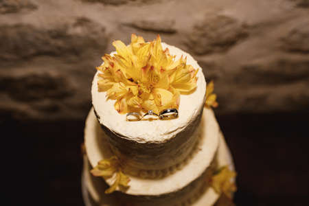 White wedding cake decorated with rings and yellow lilies. Top viewの写真素材