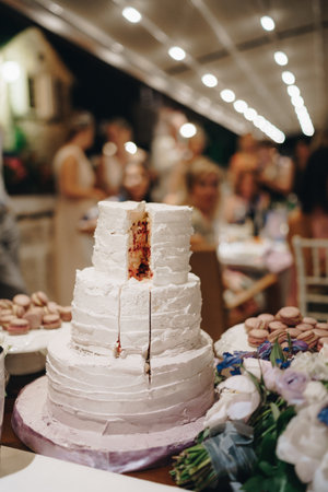 Cut wedding cake next to macaroon cakes stands on the tableの写真素材