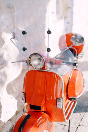 Orange motor scooter against a white stone wall