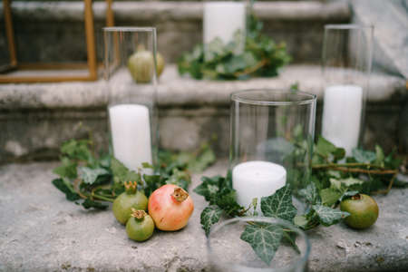 White candles in glasses stand on stone steps surrounded by pomegranates and green ivyの写真素材