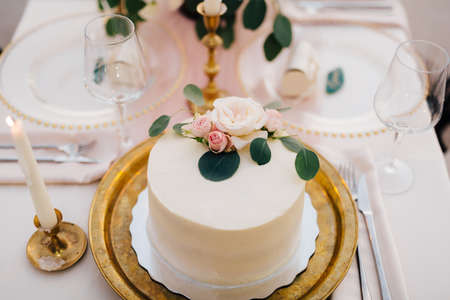 Wedding cake decorated with a rose stands on a gold plate on the tableの写真素材