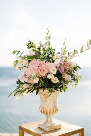 Bouquet of flowers in an antique vase stands on a stool against the background of waterの写真素材