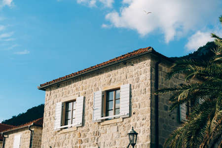 Stone facade of the building with shutters on the windows and a red tiled roof