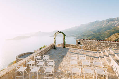 Wedding arch stands on an observation deck above the sea in front of rows of white chairsの写真素材