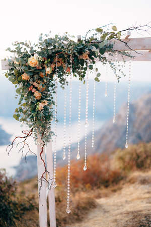 Corner of the wedding arch is decorated with roses, green branches and rows of transparent beadsの写真素材