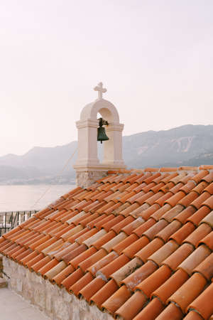 Bell on an old stone bell tower with a red tiled roof