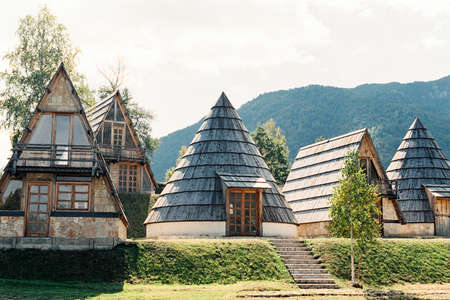 Triangular and conical houses on a lawn against the backdrop of mountains